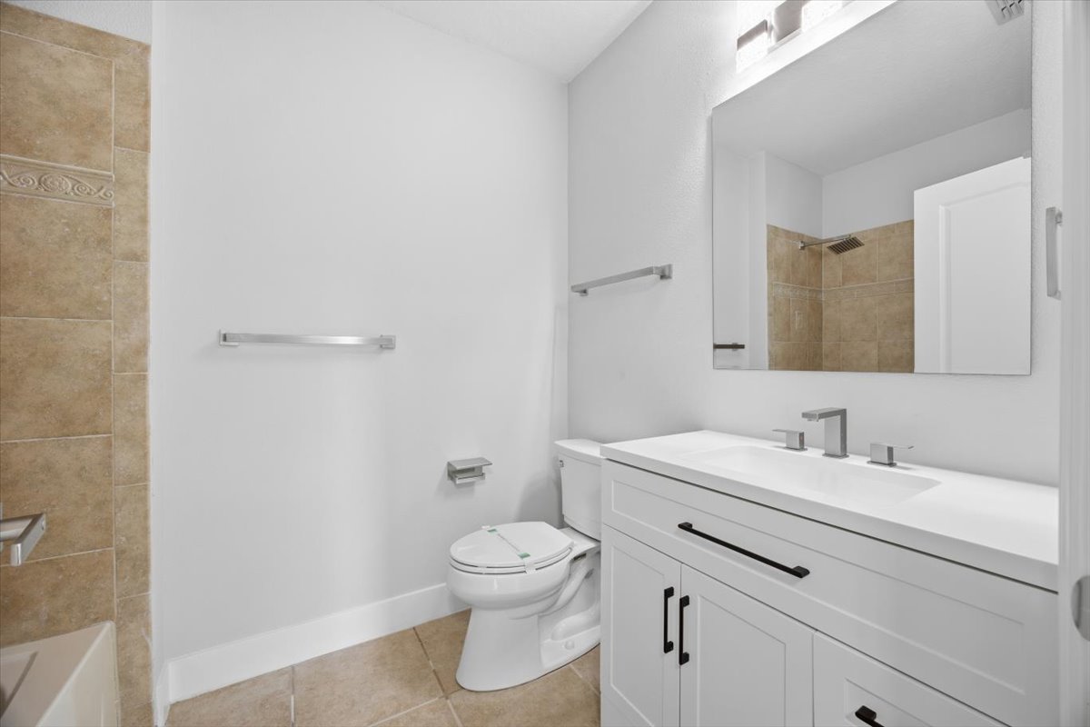 Secondary full bath with white shaker vanity and tiled tub surround